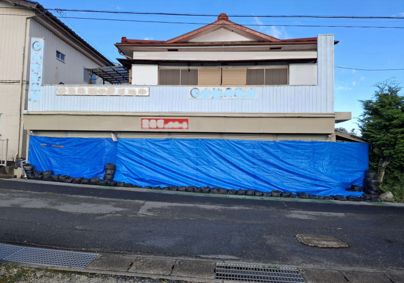 2026年9月21日に台風25号の大雨による浸水対策に、店舗シャッターからの間口14m・高さ1.8mを角型土のう袋に砂約20㎏を入れた土のうとシートを使用して防止シートを設置しました。